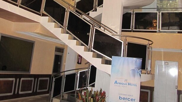 Un moderno vestíbulo de hotel con una gran araña y una escalera de caracol, y un cartel que anuncia el Hotel Afrique.