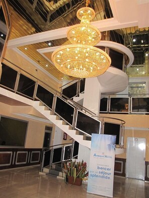 Un moderno vestíbulo de hotel con una gran araña y una escalera de caracol, y un cartel que anuncia el Hotel Afrique.