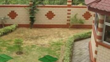 Un patio con pared de ladrillo, césped verde y un pequeño árbol.