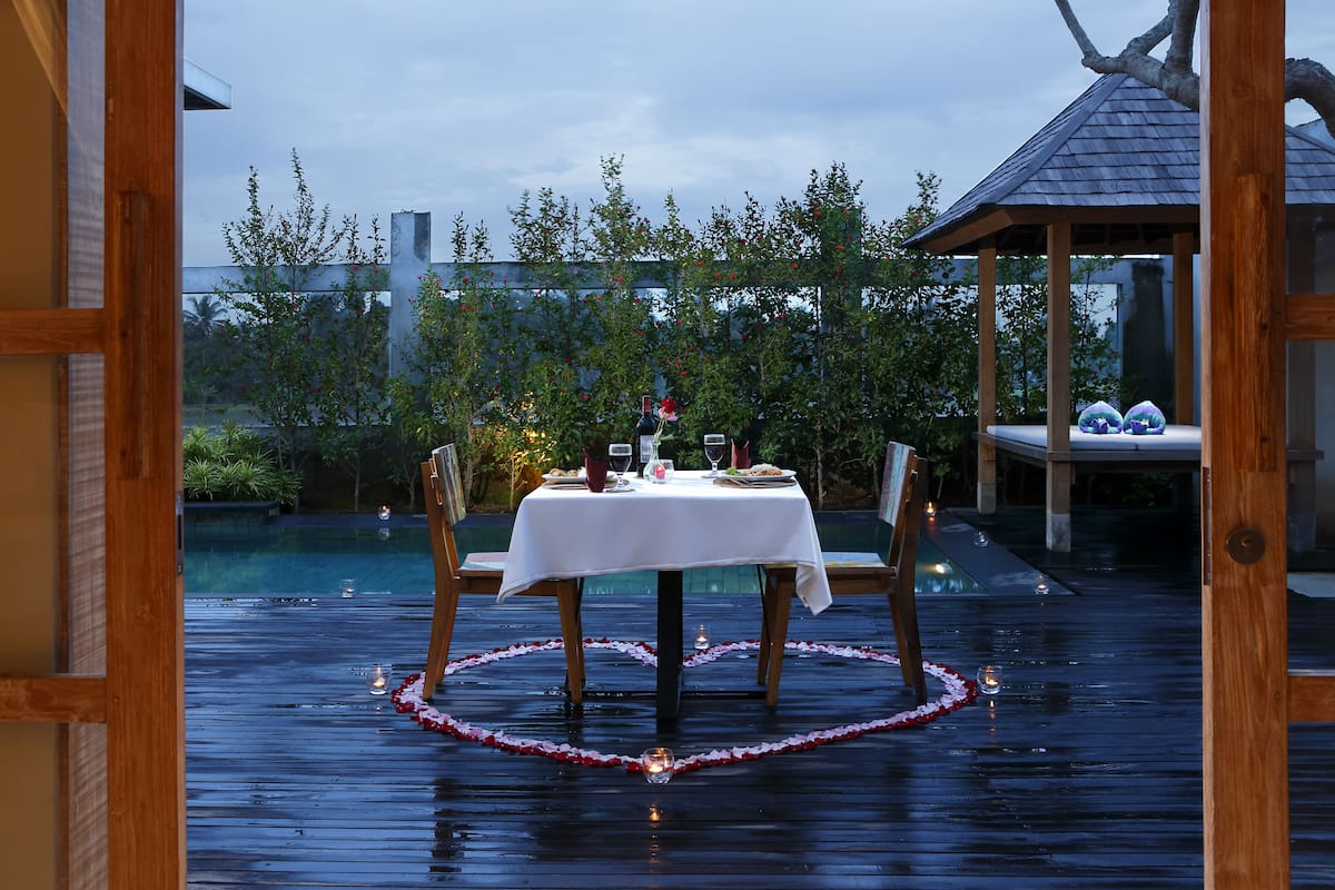 Uma área de refeições ao ar livre com uma mesa posta para dois, rodeada por um deck de madeira e uma piscina.
