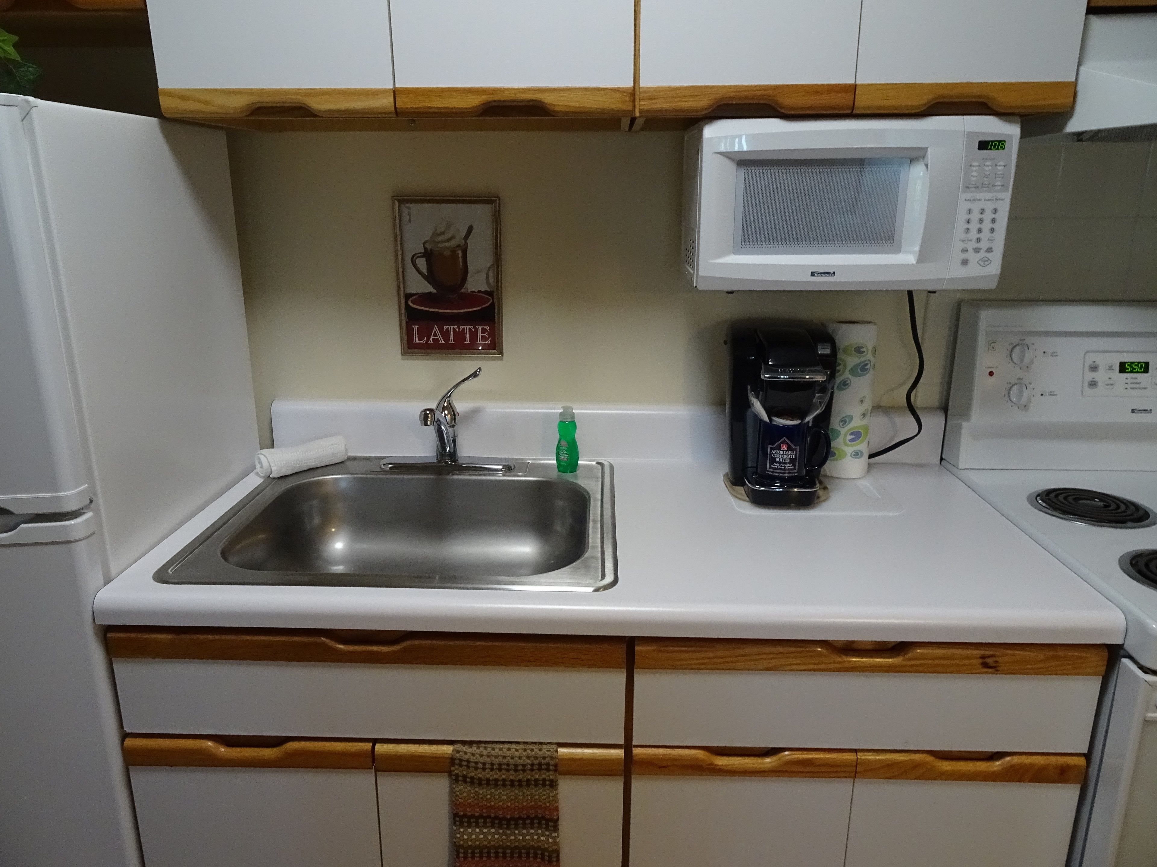A kitchen with a stainless steel sink, a microwave, a coffee maker, and wooden cabinets.