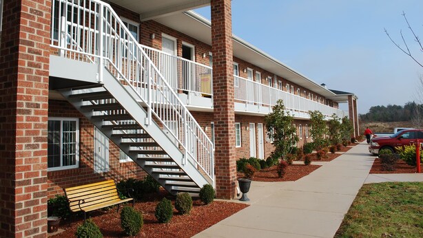 A multi-story building with a brick facade, a central staircase, and a covered walkway. - Affordable Suites Kannapolis (Kannapolis)