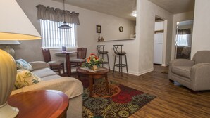 A living room with a sofa, a coffee table with flowers, a dining table, and a kitchen area in the background. - Affordable Suites Kannapolis (Kannapolis)
