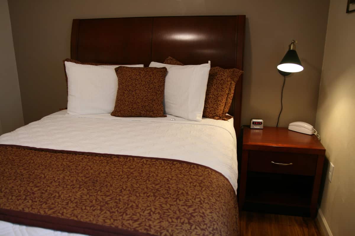 A neatly made bed with a patterned bedspread, a wooden headboard, and a bedside table with a lamp and a clock.