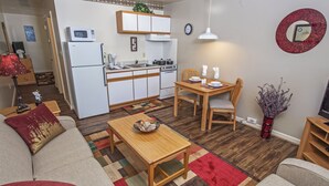 A modern kitchen with white appliances, a dining area with a wooden table and chairs, and a living room with a sofa and a coffee table. - Affordable Suites Kannapolis (Kannapolis)