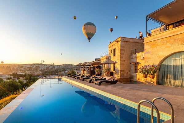 Un espace aménagé au bord de la piscine, avec des chaises longues, une vue dégagée sur la piscine et des montgolfières dans le ciel.