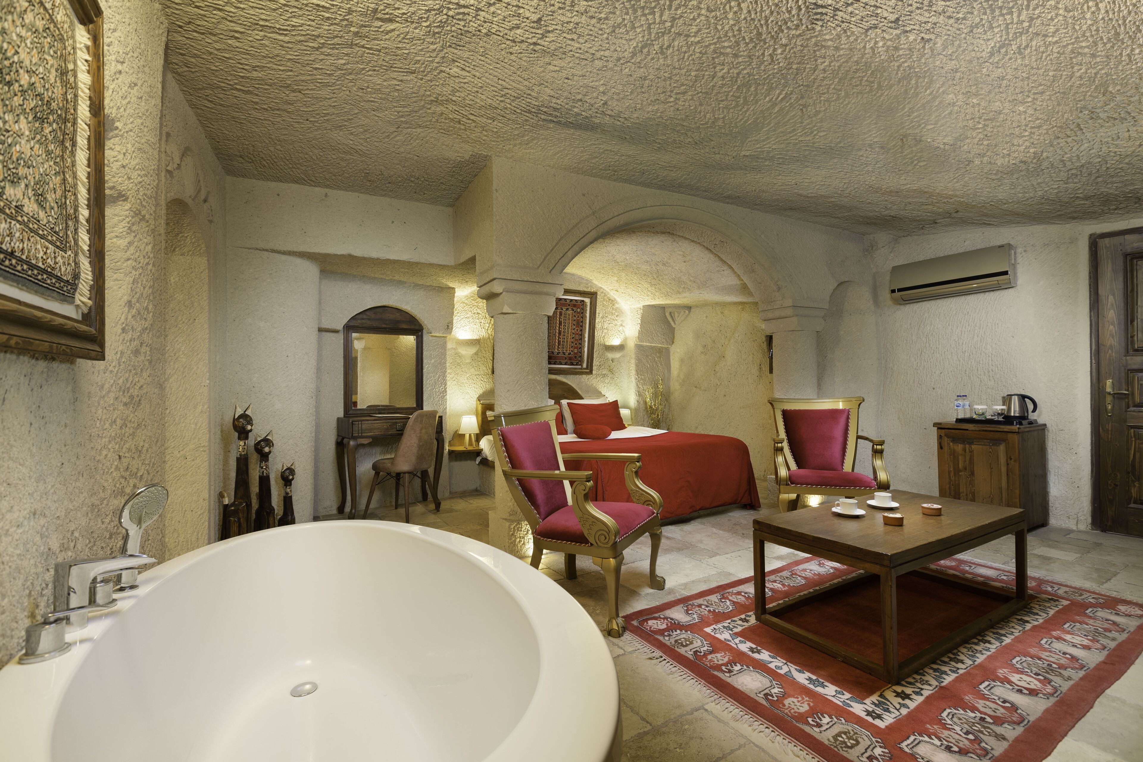 A bathroom with a large bathtub, a wooden table with cups, and a red chair.