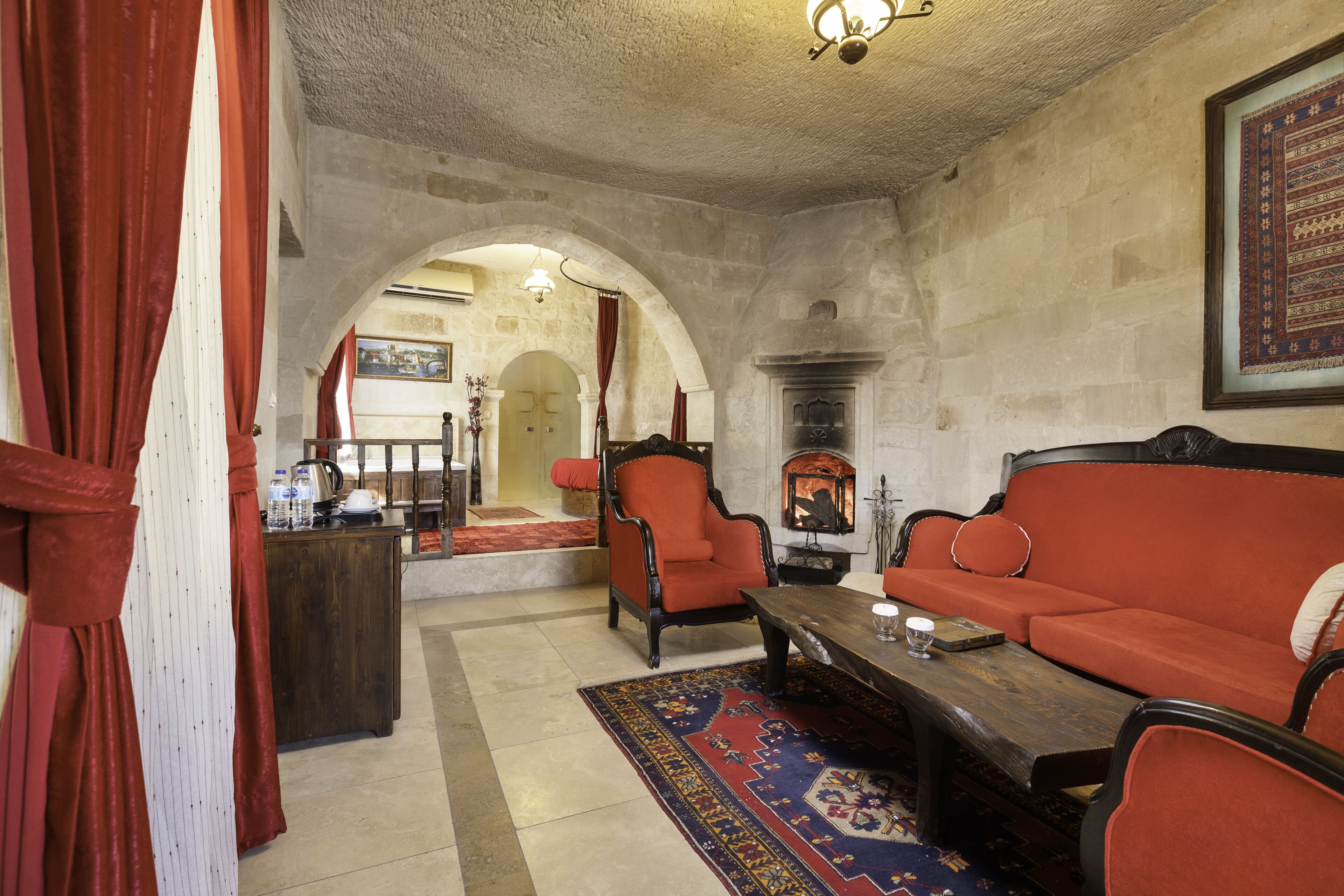 A room with a fireplace, red upholstered furniture, a wooden coffee table, and a patterned rug.