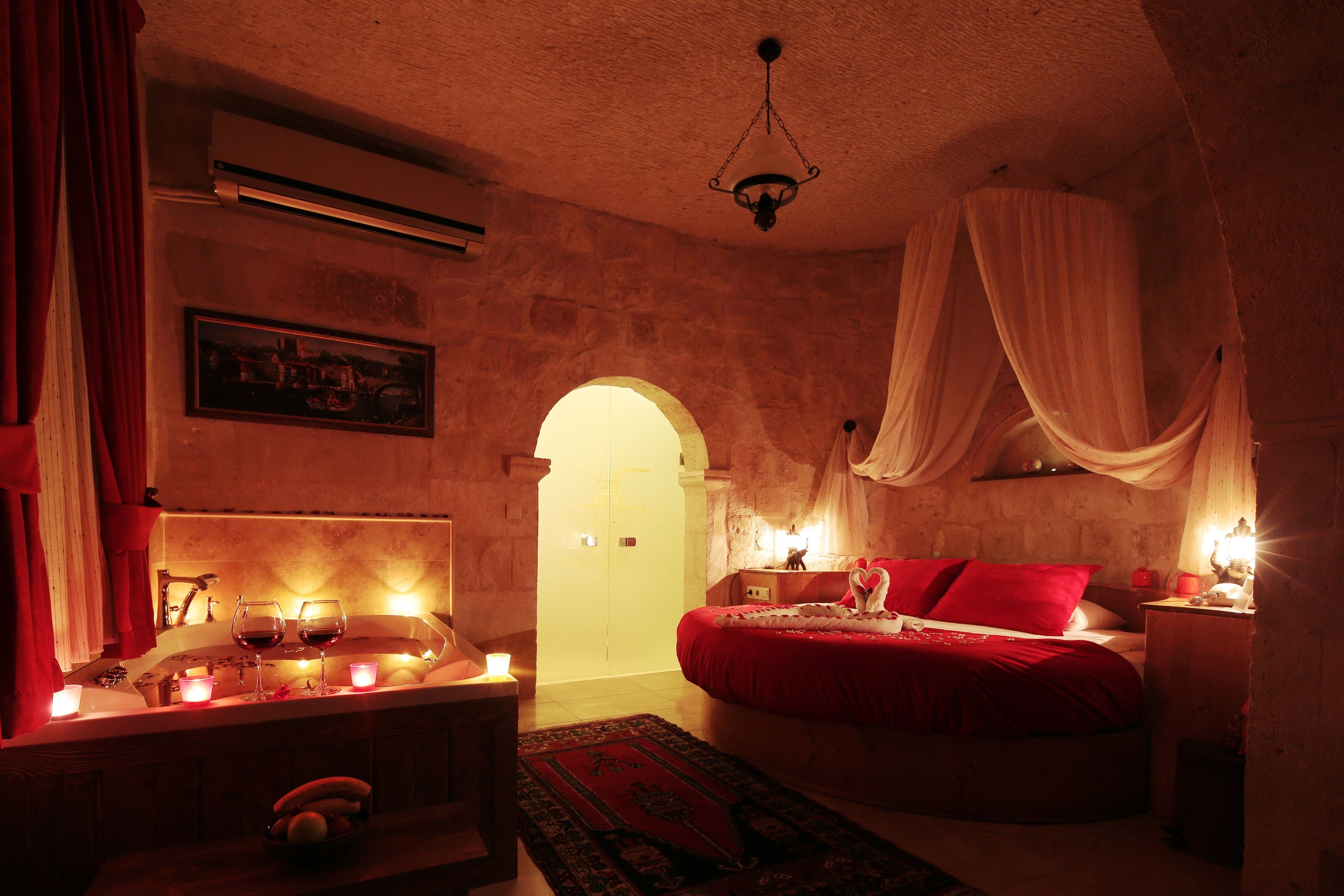 A dimly lit room with a bed, a bedside table with candles, and a red bedspread.