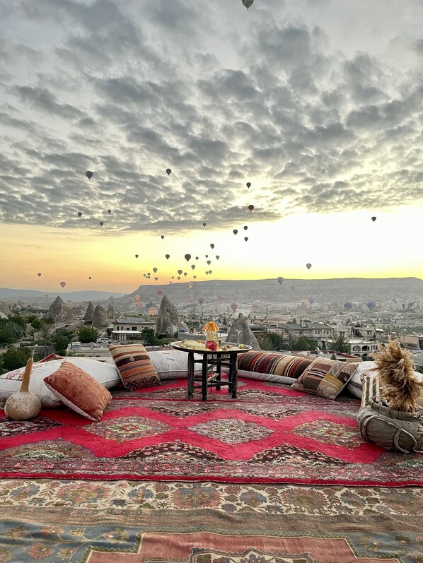 A rooftop terrace with a red carpet, cushions, and a table with a dish of food. - Doors Of Cappadocia (Nevsehir)