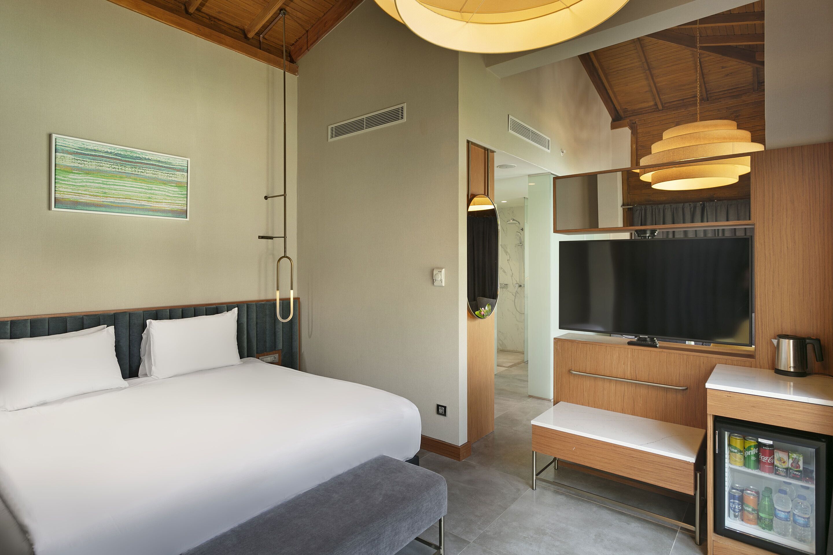 A hotel room with a large bed, a small desk with a television, and a minibar.