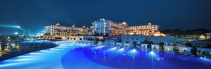 A large hotel with multiple buildings, a central pool area with blue lighting, and outdoor seating areas. - Titanic Deluxe Golf Belek (Serik)