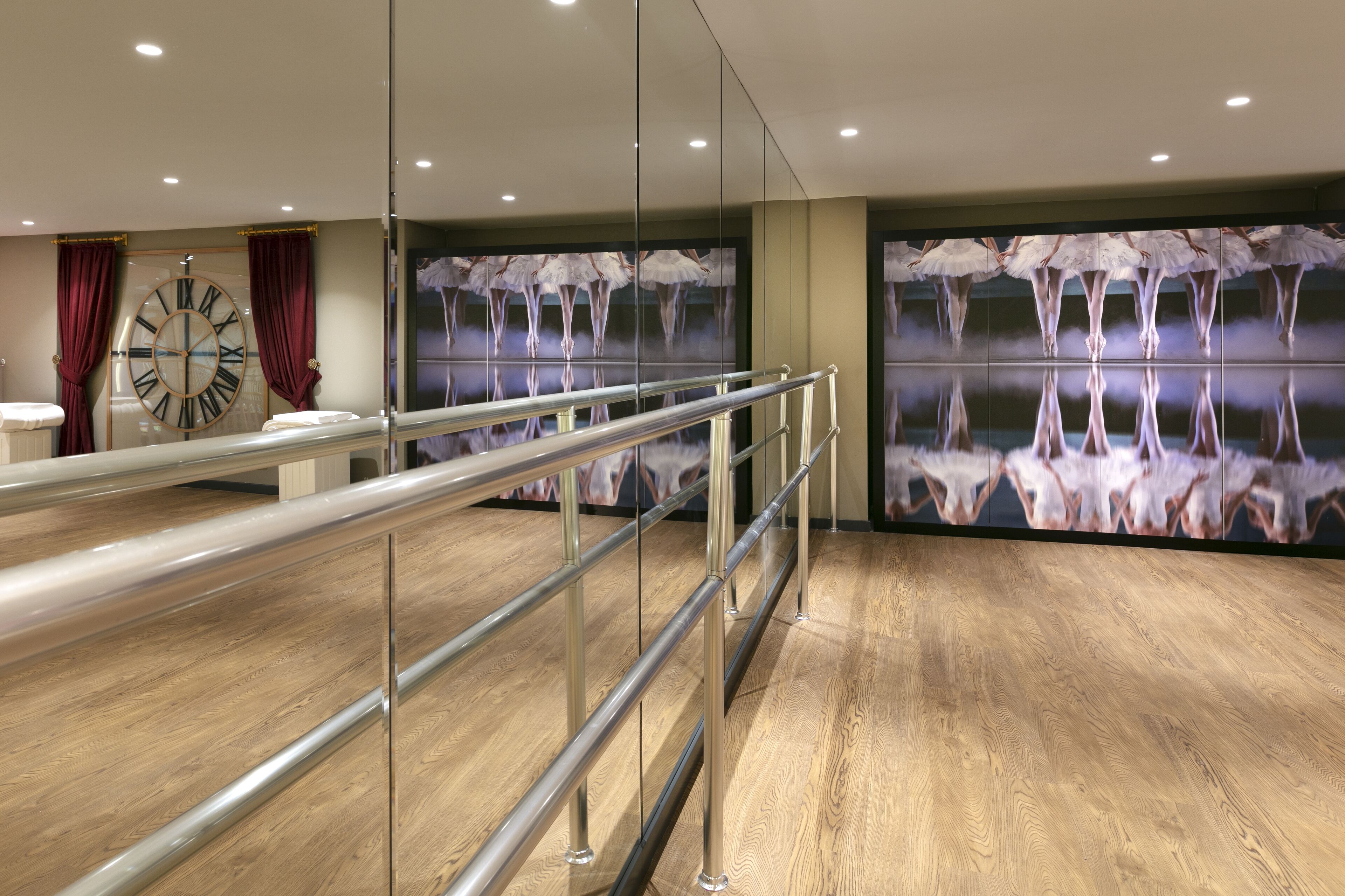 Ein Hotelzimmer mit Holzboden, einem großen Spiegel, einer Uhr und einer Wand, in der Bäume reflektiert werden.