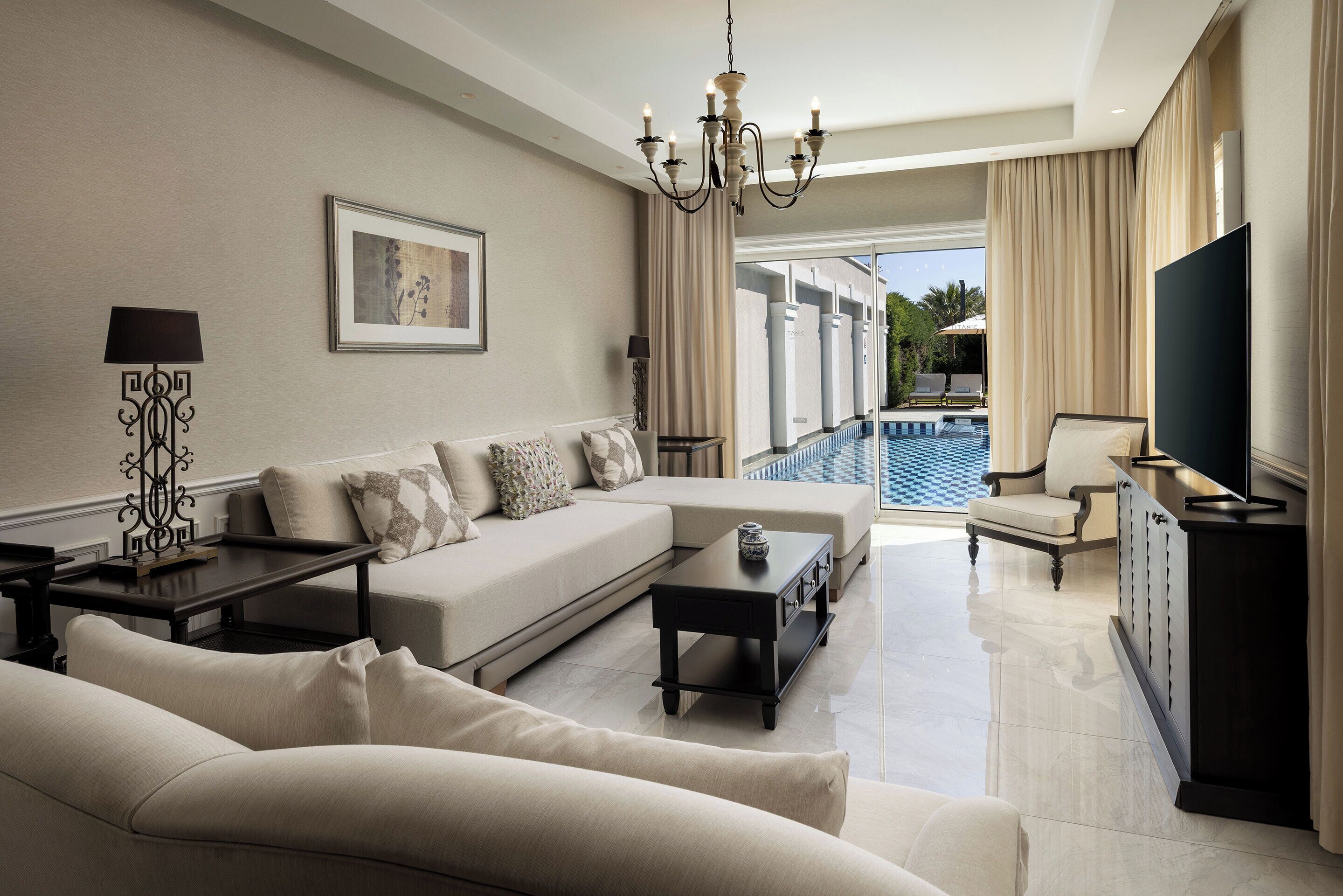 A modern living room with a sofa, coffee table, TV, and a view of a swimming pool.