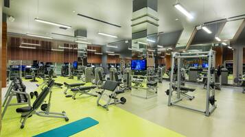 Un gimnasio moderno con varios equipos de ejercicio, espejos y múltiples pantallas de televisión.