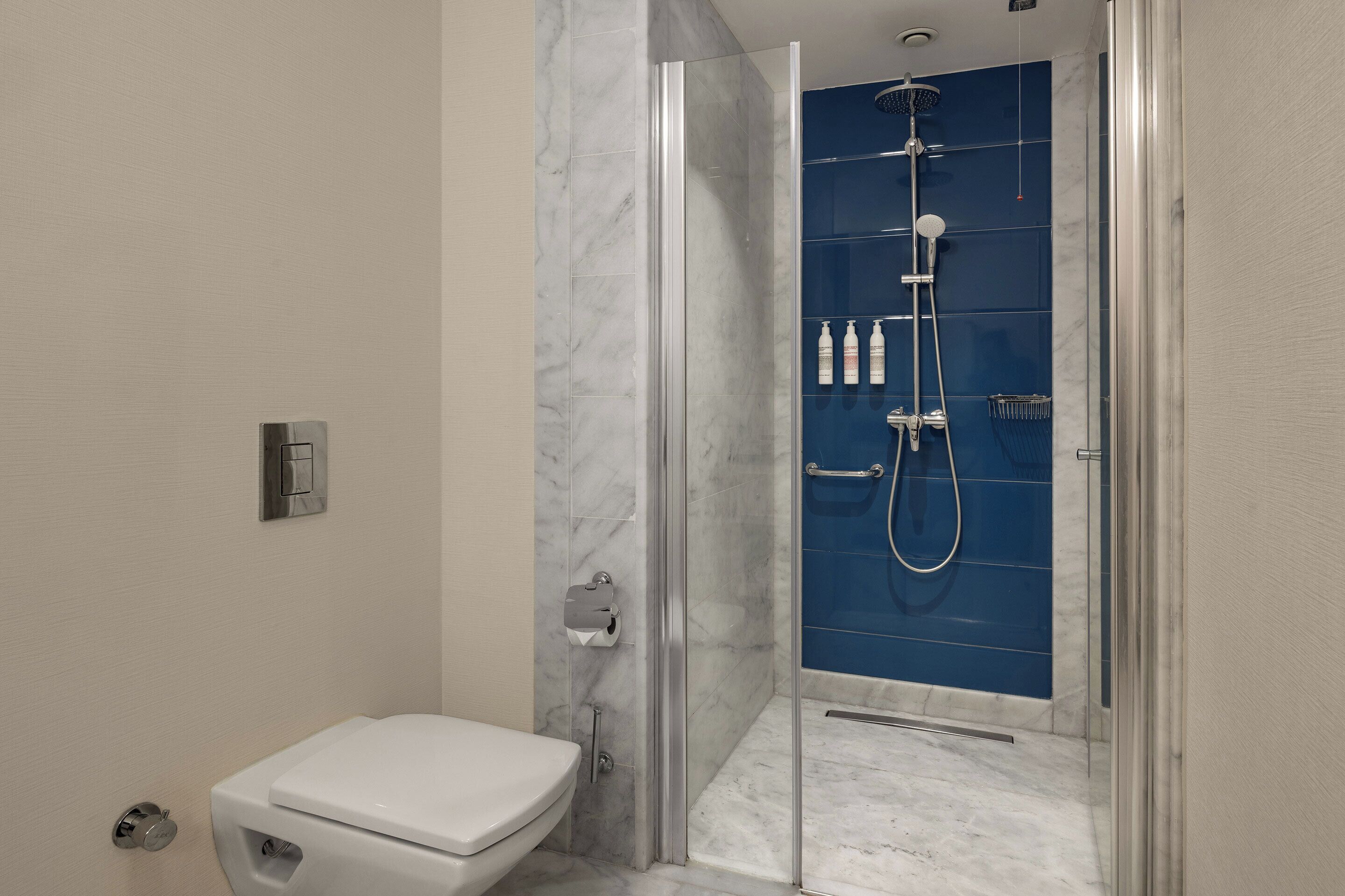 A bathroom with a toilet, a shower with a glass door, and a marble floor.