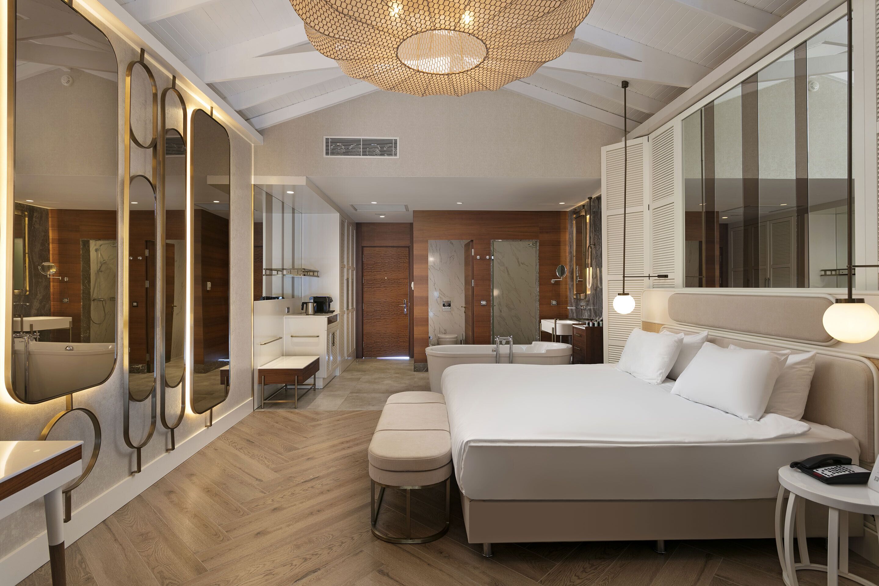 A modern hotel room with a large bed, a sitting area, a bathroom, and a large mirror.