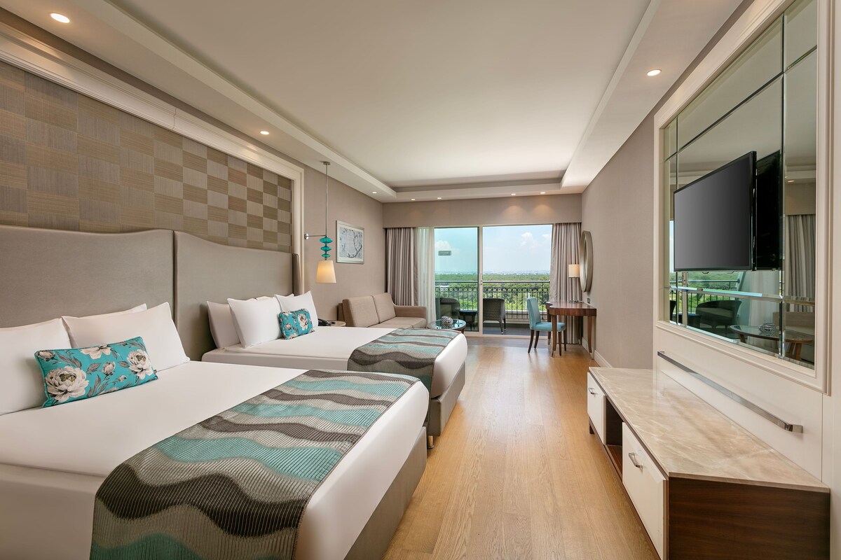 A hotel room with two beds, a TV, a desk, and a view of the outdoors.