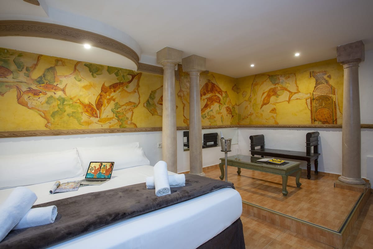 Una habitación de hotel con una cama, un escritorio, una silla, una computadora portátil y un mural en la pared.
