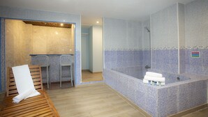 A modern bathroom with a wooden bench, a bathtub, and a shower area. - Casual de las Civilizaciones Valencia by Casual Hoteles (Valencia)