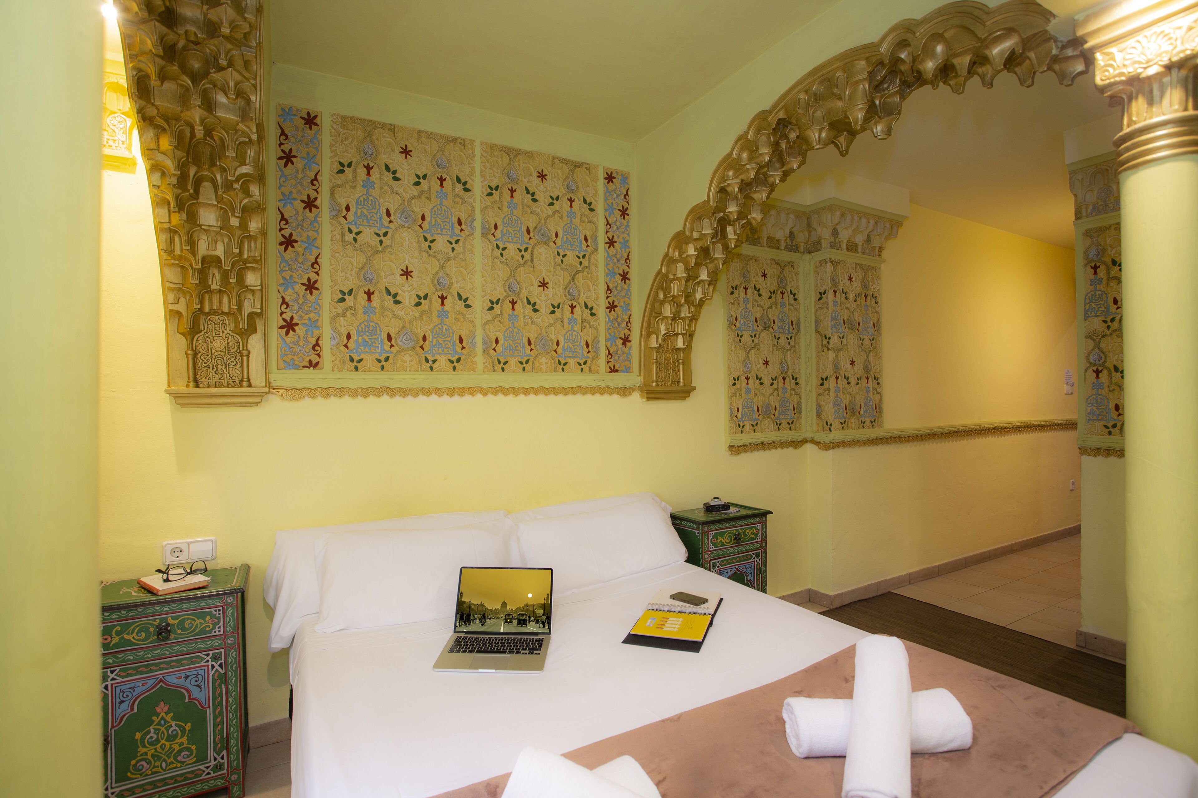 A hotel room with a bed, a laptop, a notebook, and a decorative mirror.