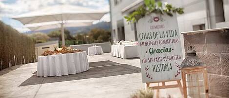 An outdoor event space with tables set up for dining, a sign with a message, and potted plants.