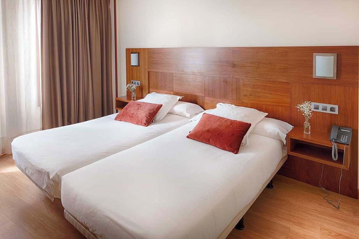 A double bed with two pillows, a wooden headboard, bedside tables with lamps, and a telephone.