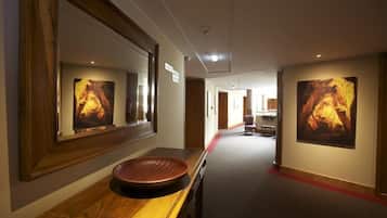 A hallway with a wooden vanity, large framed artwork on the walls, and a red carpet.