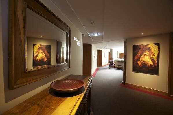 A hallway with a wooden vanity, large framed artwork on the walls, and a red carpet. - Hotel Zalle Don Fernando (Siero)