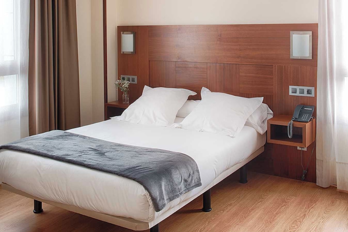 Habitación de hotel con una cama grande, un teléfono en la mesita de noche y una pequeña mesa con un florero.