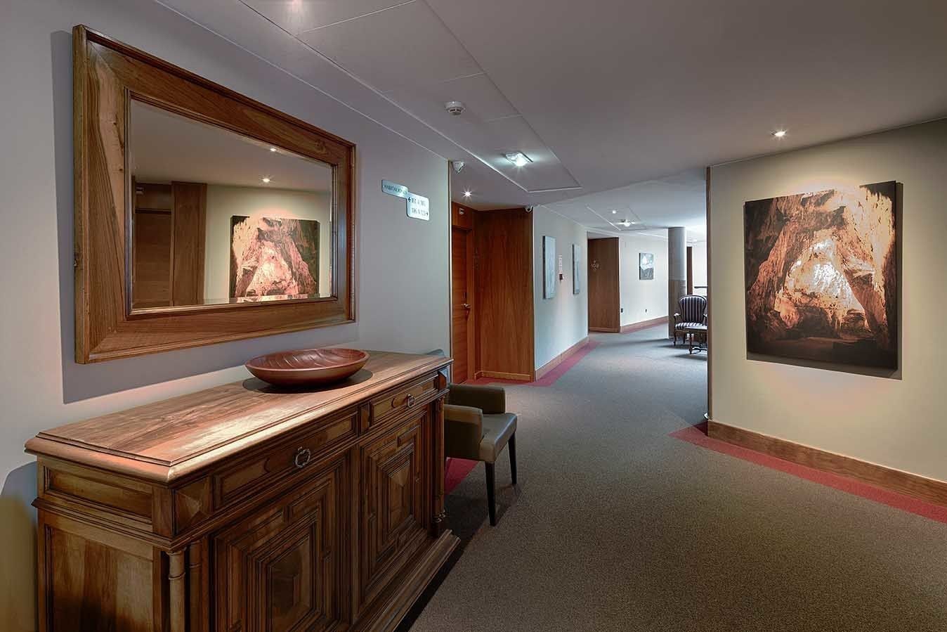 A hallway with a wooden vanity, a large mirror, and a bowl on the counter. There are framed pictures on the walls and a carpeted floor.