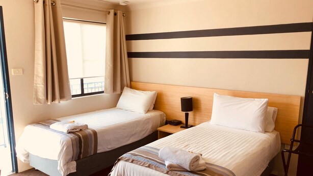 Ein Hotelzimmer mit zwei Betten, einem Fenster mit Vorhängen, einem Nachttisch mit Lampe und einem Sessel.