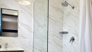 A modern bathroom with a glass-enclosed shower, a wooden vanity, and a marble-tiled floor.
