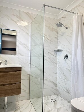 A modern bathroom with a glass-enclosed shower, a wooden vanity, and a marble-tiled floor.