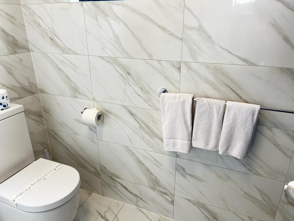 A bathroom with a toilet, marble tiles, and two towels hanging on a rack.