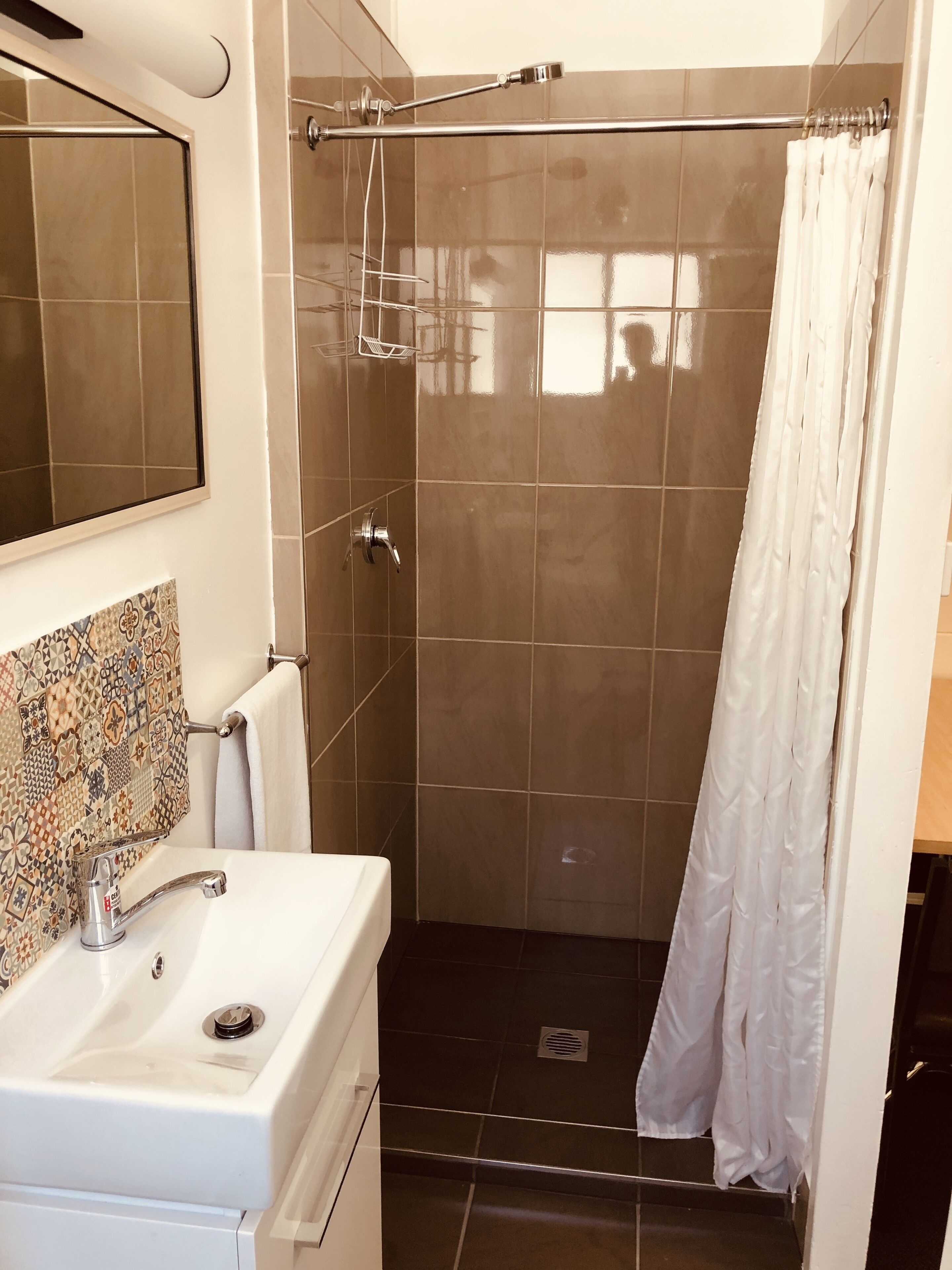 Ein Badezimmer mit Waschbecken, Spiegel, Dusche und Fliesenwänden.