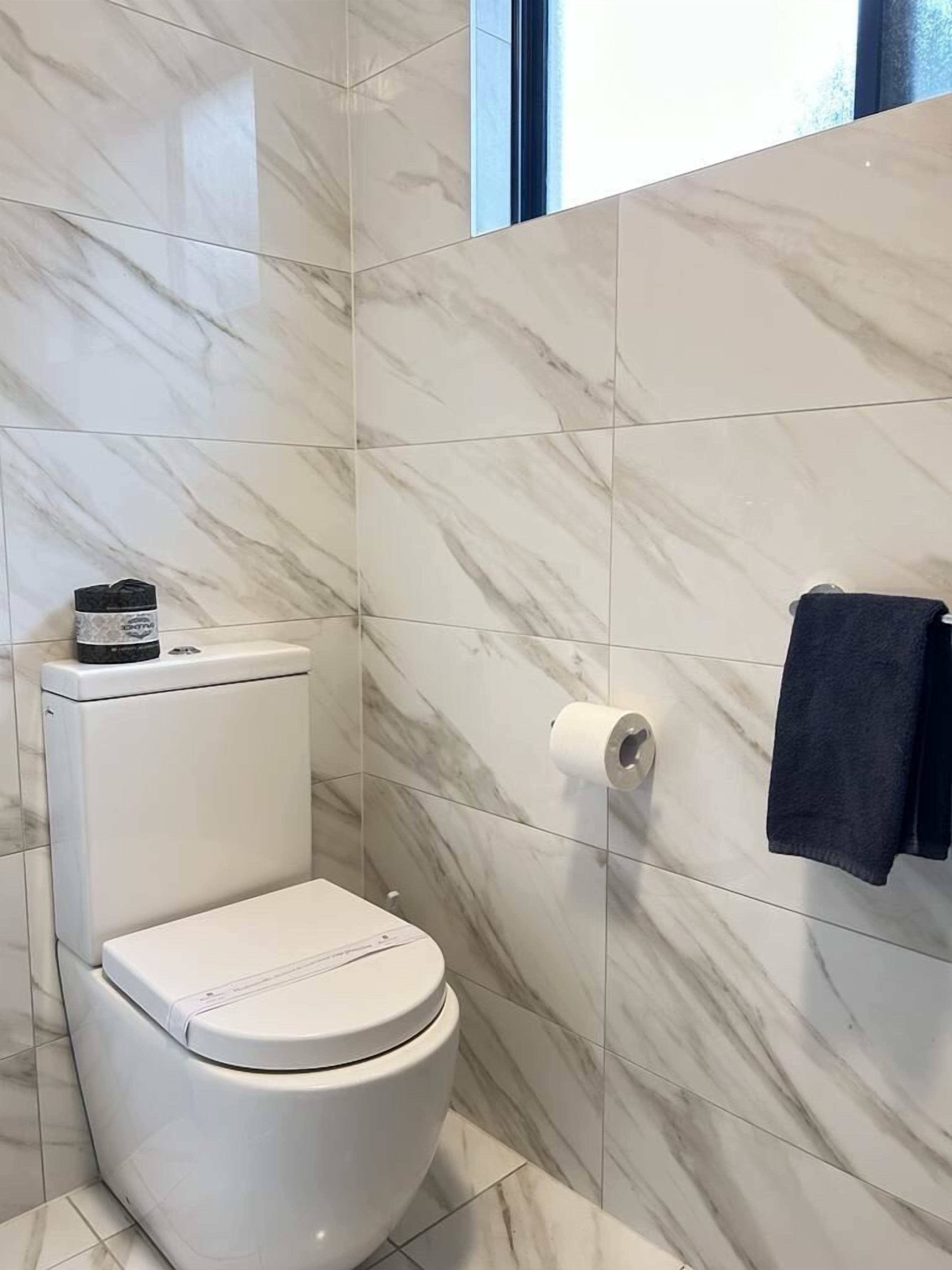Un baño con inodoro, un dispensador de papel higiénico y una toalla colgada en la pared.