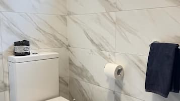 Un baño con inodoro, un dispensador de papel higiénico y una toalla colgada en la pared.
