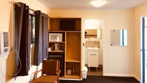 Ein kleines Zimmer mit Bett, Fernseher, Mikrowelle, einer kleinen Küchenzeile und einem Sessel.