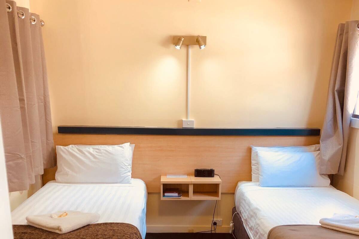 Ett hotellrum med två sängar, ett nattduksbord, en lampa och ett fönster med gardiner.