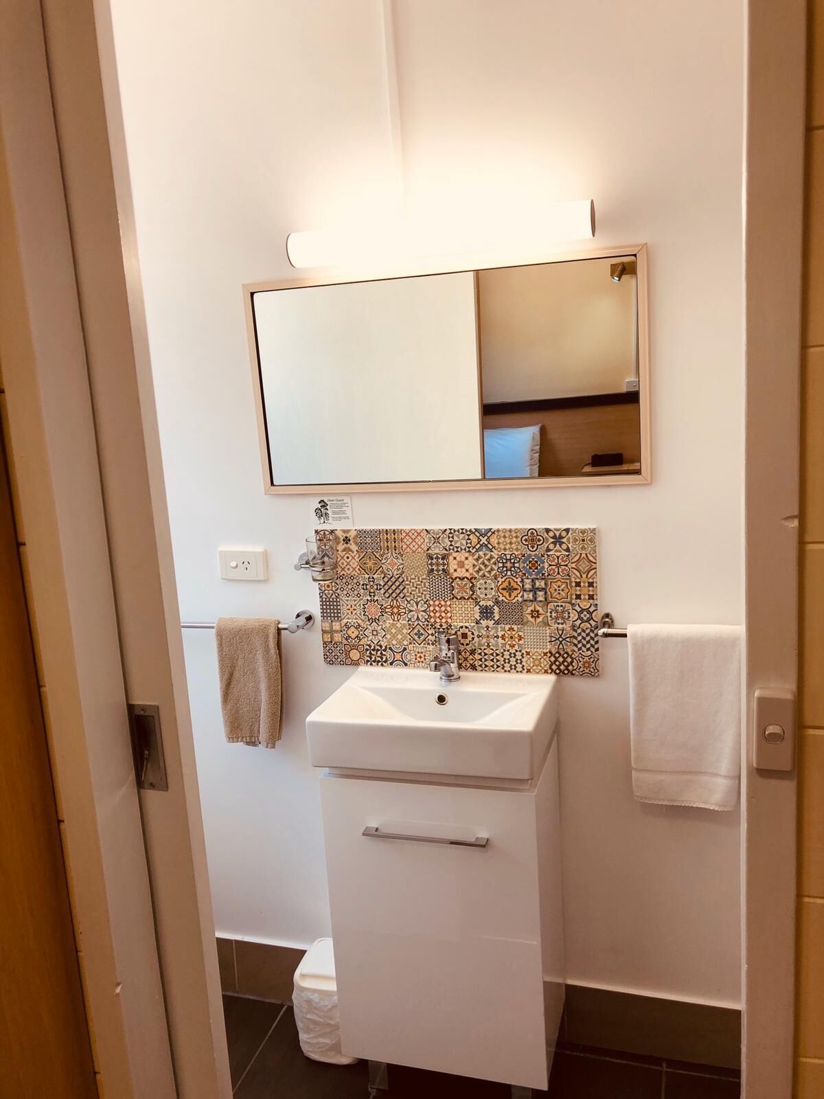 Un baño con lavabo blanco, espejo y salpicadero de azulejos estampados.