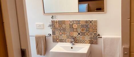 Un baño con lavabo blanco, espejo y salpicadero de azulejos estampados.