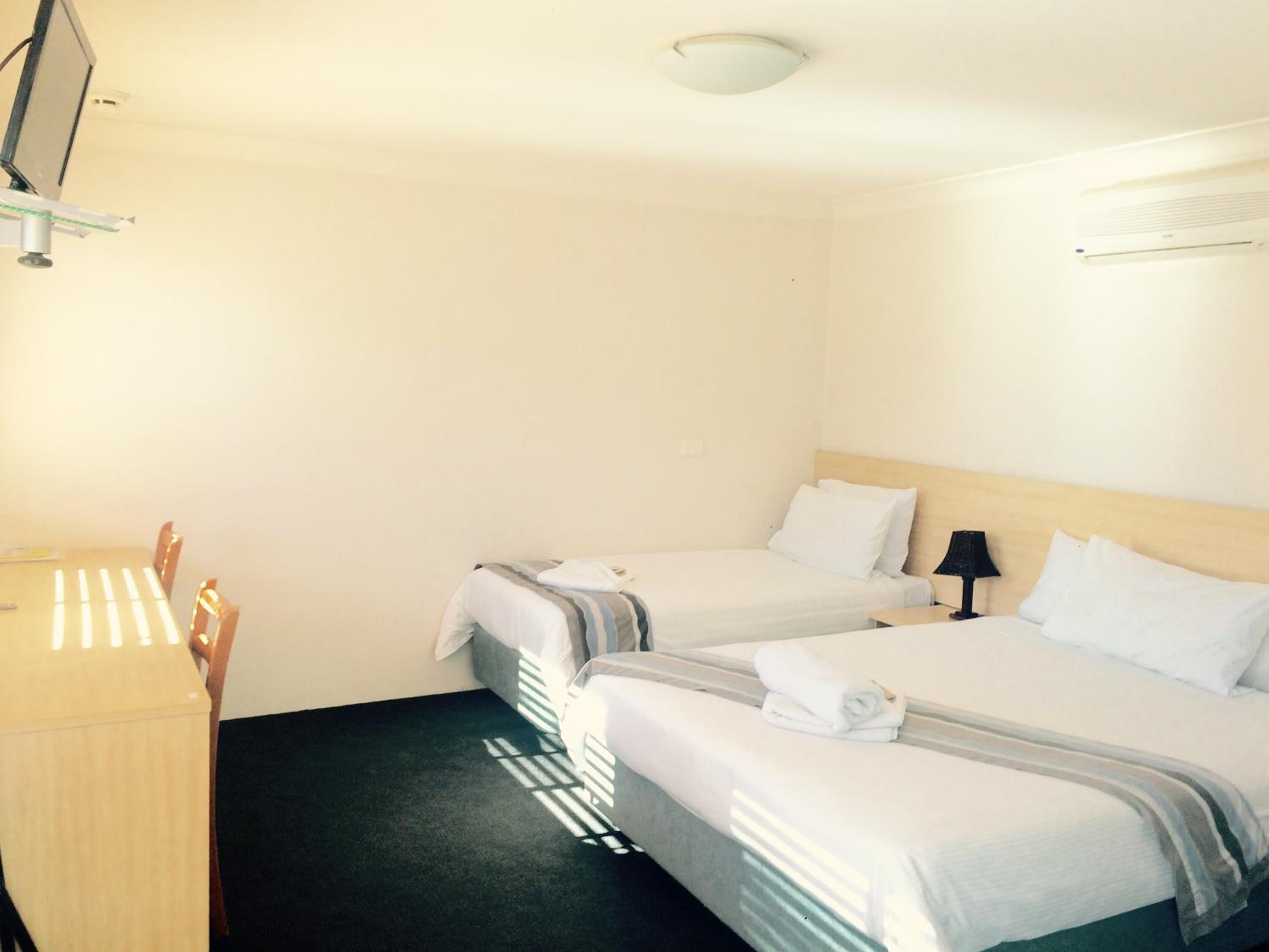 A hotel room with two beds, a desk, a lamp, and a ceiling light.