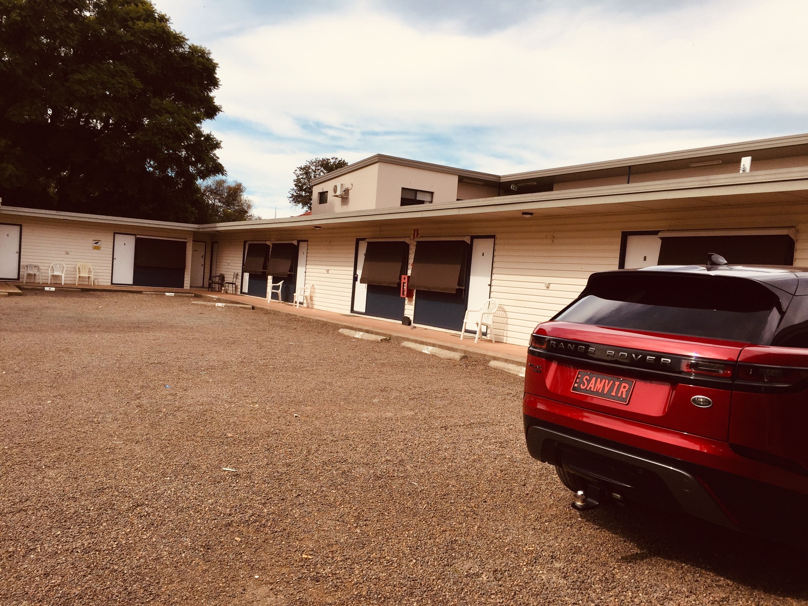 A building with multiple doors and windows, a gravel driveway, and a parked red car.