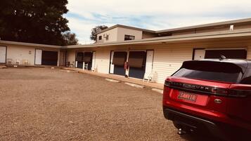 A building with multiple doors and windows, a gravel driveway, and a parked red car.