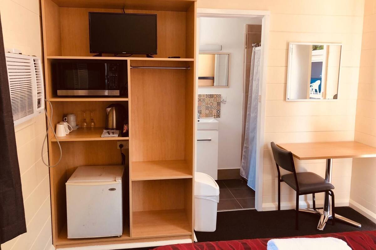 Ett litet rum med tv, ett litet kök och ett skrivbord med en stol.