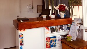 Ein Empfangsbereich mit einer Uhr, einem Fenster mit Jalousien, einer Vase mit Blumen und verschiedenen Informationsplakaten.
