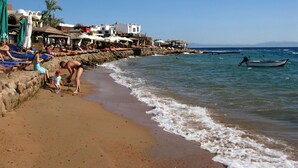 A beach with a rocky shoreline, a small boat, and people relaxing on the sand. - Red Sea Relax (Dahab)