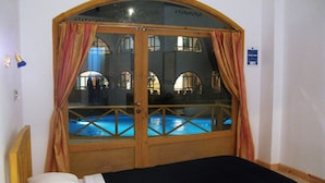 A room with a bed, a wooden door with glass panels, and a view of a pool through the door. - Red Sea Relax (Dahab)