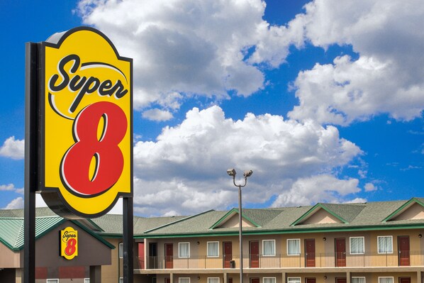 Um motel Super 8 com uma placa chamativa, um edifício de dois andares e um céu azul claro com nuvens.